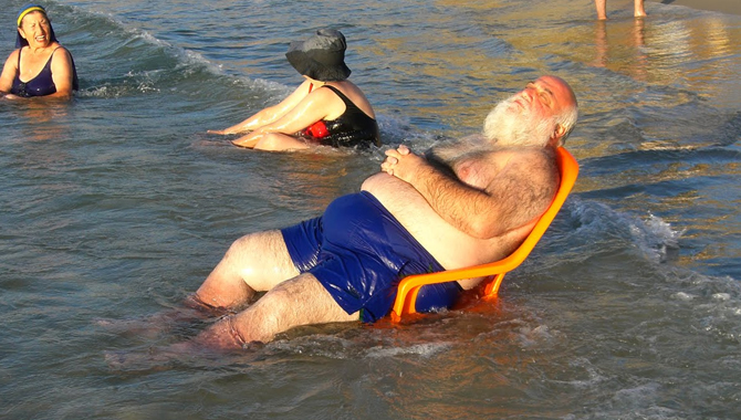 Fat Old Man Balancing On A Chair In The Sea