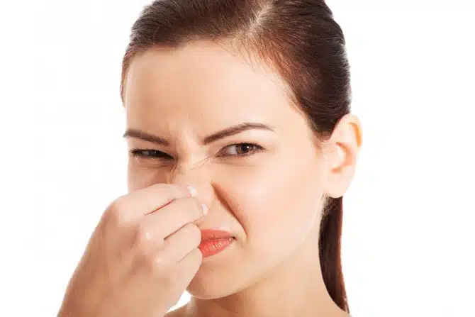 Portrait of a young woman holding her nose because of a bad smel