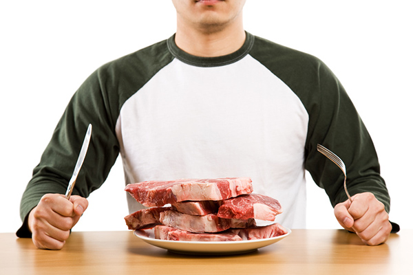 A hungry man holding a knife and a fork ready to eat a stack of raw steak