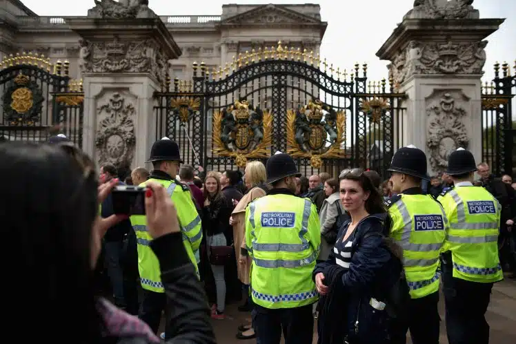 LONDON, UNITED KINGDOM - MAY 02: Tourists pose for photographs as Metropolitan Police officers keep an eye on the thousands of people lined up for a chance to glimpse and photograph the announcement of the birth of Prince William, Duke of Cambridge and the Duchess of Cambridge's second child outside Buckingham Palace on May 2, 2015 in London, United Kingdom. Catherine, Duchess of Cambridge delivered the baby girl at 8:34am Saturday and she is the fourth in line to the throne and the Queen's fifth great-grandchild. (Photo by Chip Somodevilla/Getty Images)