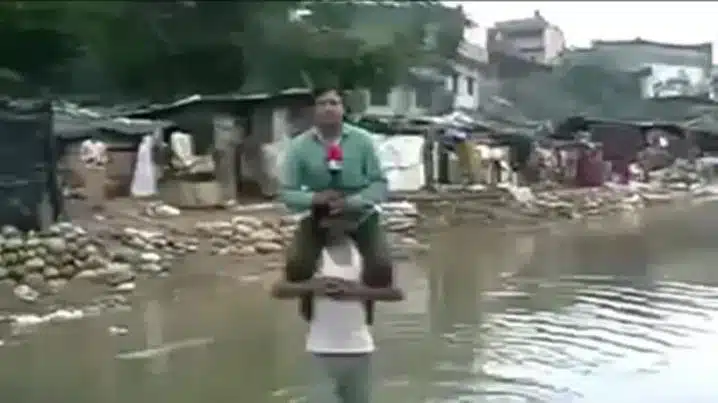 Indian News Reporter Narayan Pargaien Uses Flood Victim To Keep Himself Dry While Reporting