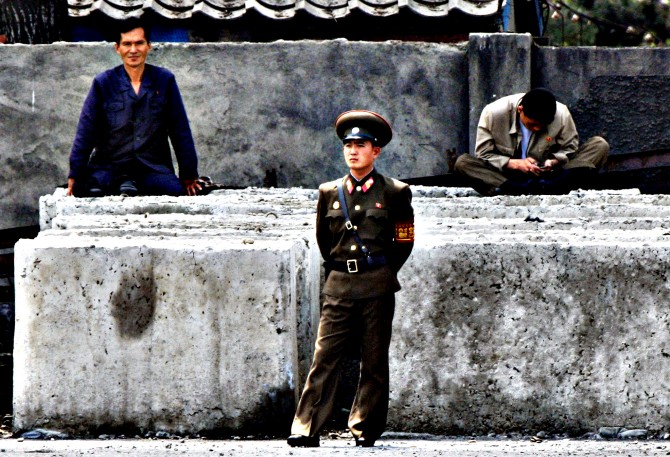 A North Korean worker checks his mobile phone as a soldier stand