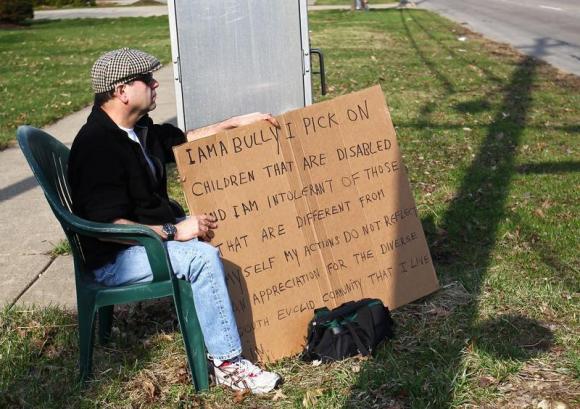 Aviv sits with an "I am a bully" sign at a street corner in the Cleveland suburb of South Euclid