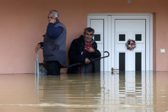 Two men stand in the waters in front of their flooded house as they wait to be evacuated in the town of Obrenovac, east from Belgrade
