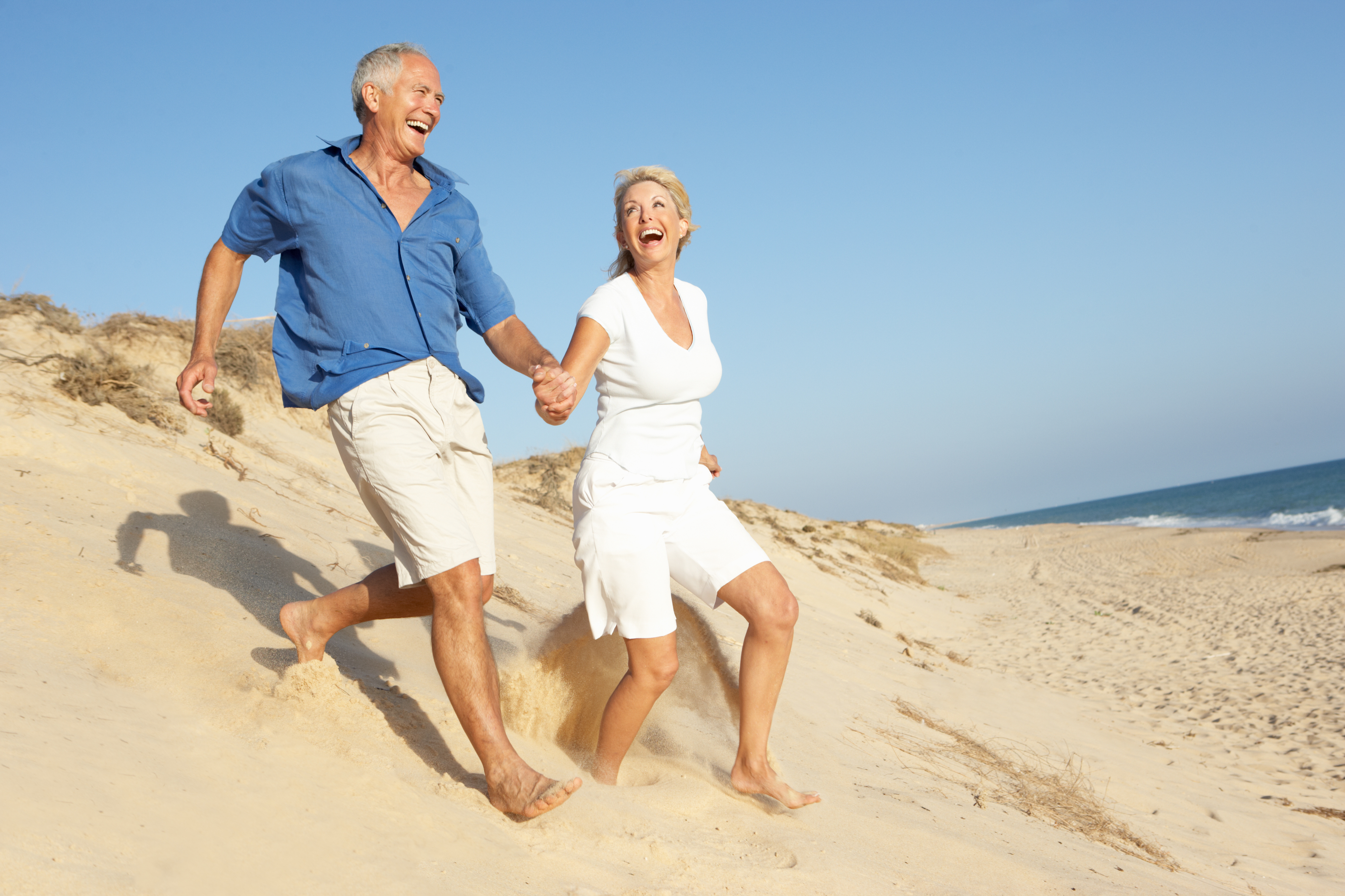 Senior Couple Enjoying Beach Holiday Running Down Dune