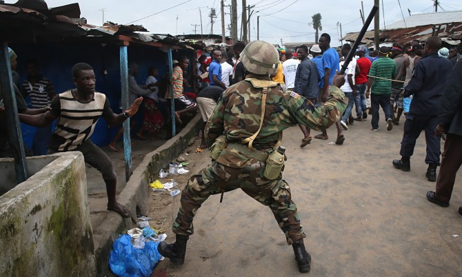 A Liberian army soldier beats a local resident while enforcing a quarantine on the West Point slum