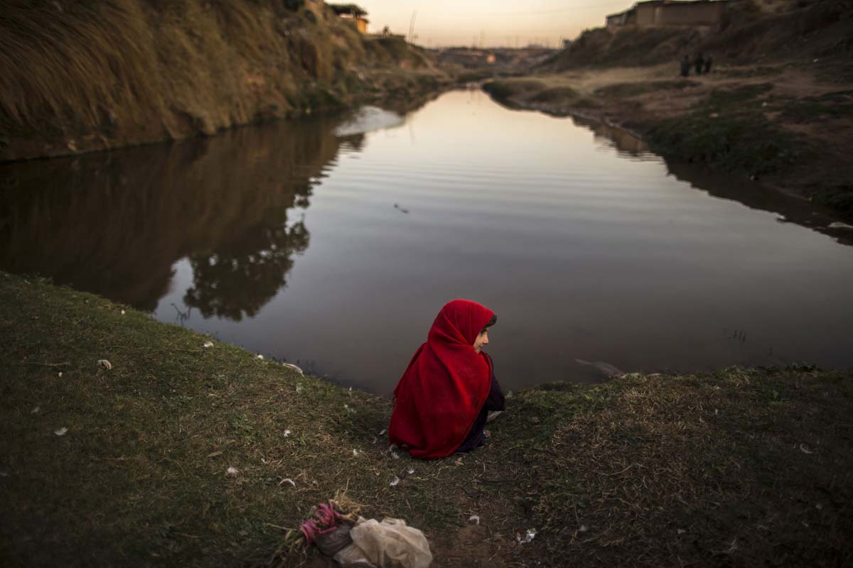A girl sits at the edge of a stream in a slum on the outskirts of Islamabad