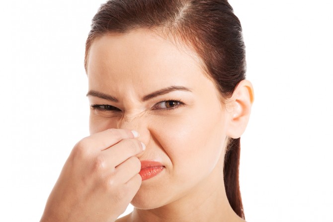 Portrait of a young woman holding her nose because of a bad smel