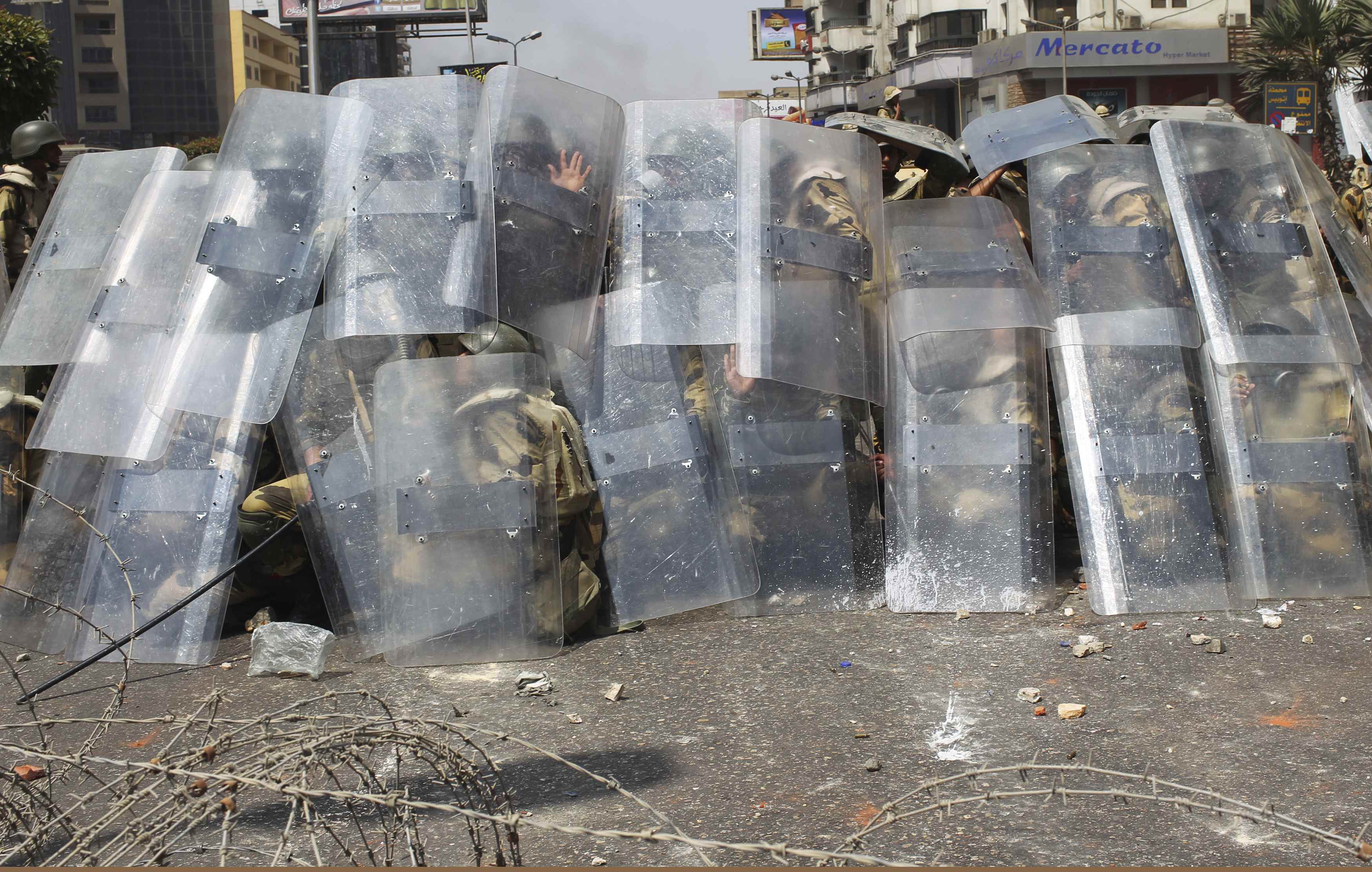 Riot police and army soldiers protect themselves with riot shields as members of the Muslim Brotherhood and supporters of ousted Egyptian President Mursi throw stones during clashes around the area of Rabaa Adawiya square