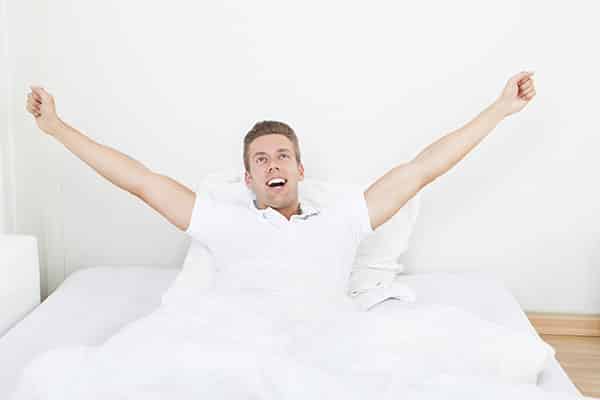 Young Man Waking Up In Morning And Stretching On Bed