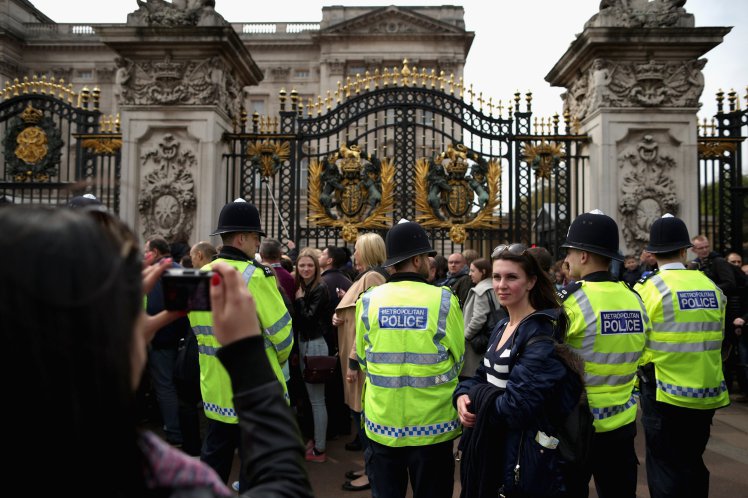 LONDON, UNITED KINGDOM - MAY 02: Tourists pose for photographs as Metropolitan Police officers keep an eye on the thousands of people lined up for a chance to glimpse and photograph the announcement of the birth of Prince William, Duke of Cambridge and the Duchess of Cambridge's second child outside Buckingham Palace on May 2, 2015 in London, United Kingdom. Catherine, Duchess of Cambridge delivered the baby girl at 8:34am Saturday and she is the fourth in line to the throne and the Queen's fifth great-grandchild. (Photo by Chip Somodevilla/Getty Images)