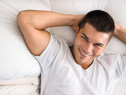 High angle view of handsome Caucasian mid adult man lying with hands behind head smiling.