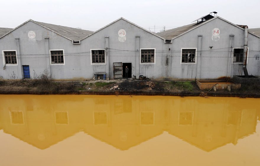 A worker looks at a photographer from a door of a factory manufacturing screws and nuts next to a polluted river in Jiaxing, Zhejiang province March 15, 2012. China's continuing reliance on heavy industry meant it failed to meet its own targets for cleaning its air and water in 2011, the head of the top planning agency told journalists on Monday. REUTERS/Stringer (CHINA - Tags: ENVIRONMENT BUSINESS) CHINA OUT. NO COMMERCIAL OR EDITORIAL SALES IN CHINA - RTR2ZD8N