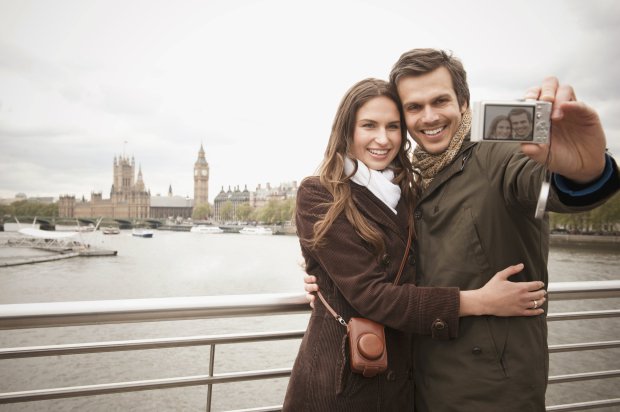 Couple taking selfie on urban bridge near city skyline, London, Middlesex, United Kingdom