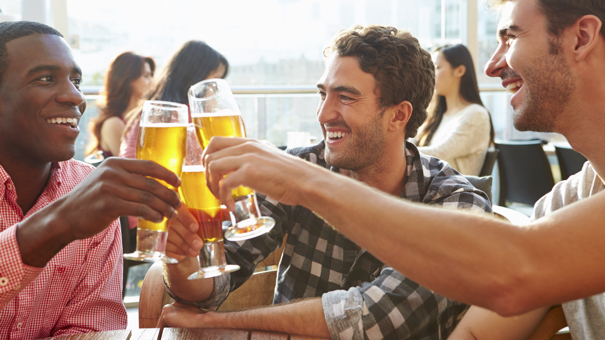 Three Male Friends Enjoying Drink At Outdoor Rooftop Bar