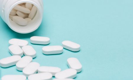 Medication bottle and white pills spilled over blue pastel colored background. Medication and prescription pills background. Pharmaceutical drugs.