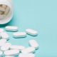 Medication bottle and white pills spilled over blue pastel colored background. Medication and prescription pills background. Pharmaceutical drugs.