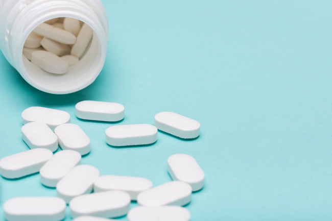 Medication bottle and white pills spilled over blue pastel colored background. Medication and prescription pills background. Pharmaceutical drugs.